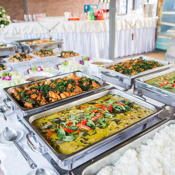 Buffet line with several chafing dishes filled with various Asian-inspired dishes, including green curry and rice.