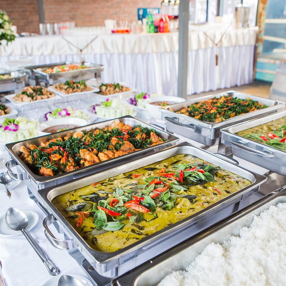 Buffet line with several chafing dishes filled with various Asian-inspired dishes, including green curry and rice.