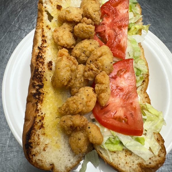 A fried shrimp po'boy sandwich with lettuce and tomato on a white plate.