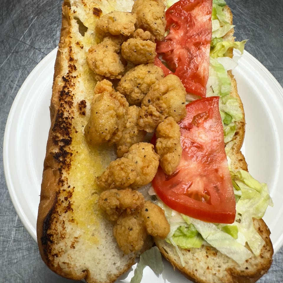 A fried shrimp po'boy sandwich with lettuce and tomato on a white plate.