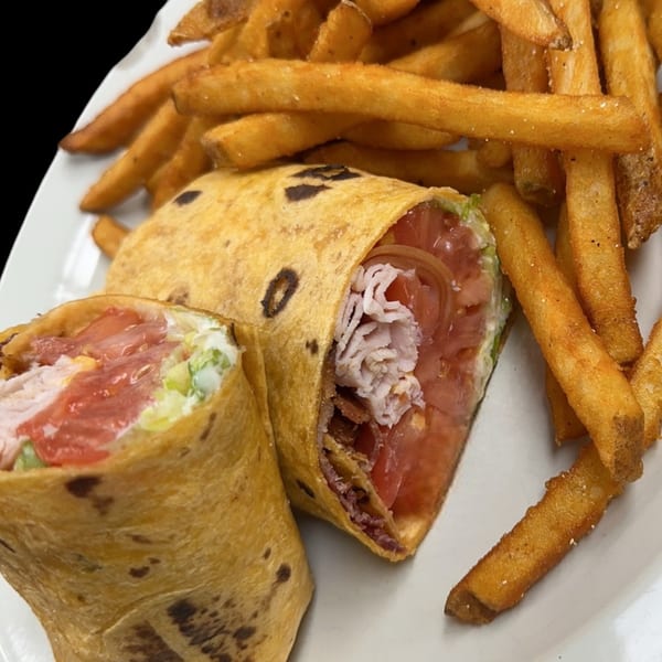 A turkey and bacon wrap, cut in half, served with a side of golden french fries.