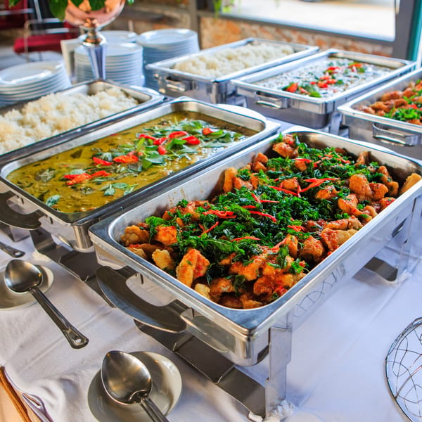 Buffet line with chafing dishes of green curry, rice, and a stir-fry with basil and chilies.