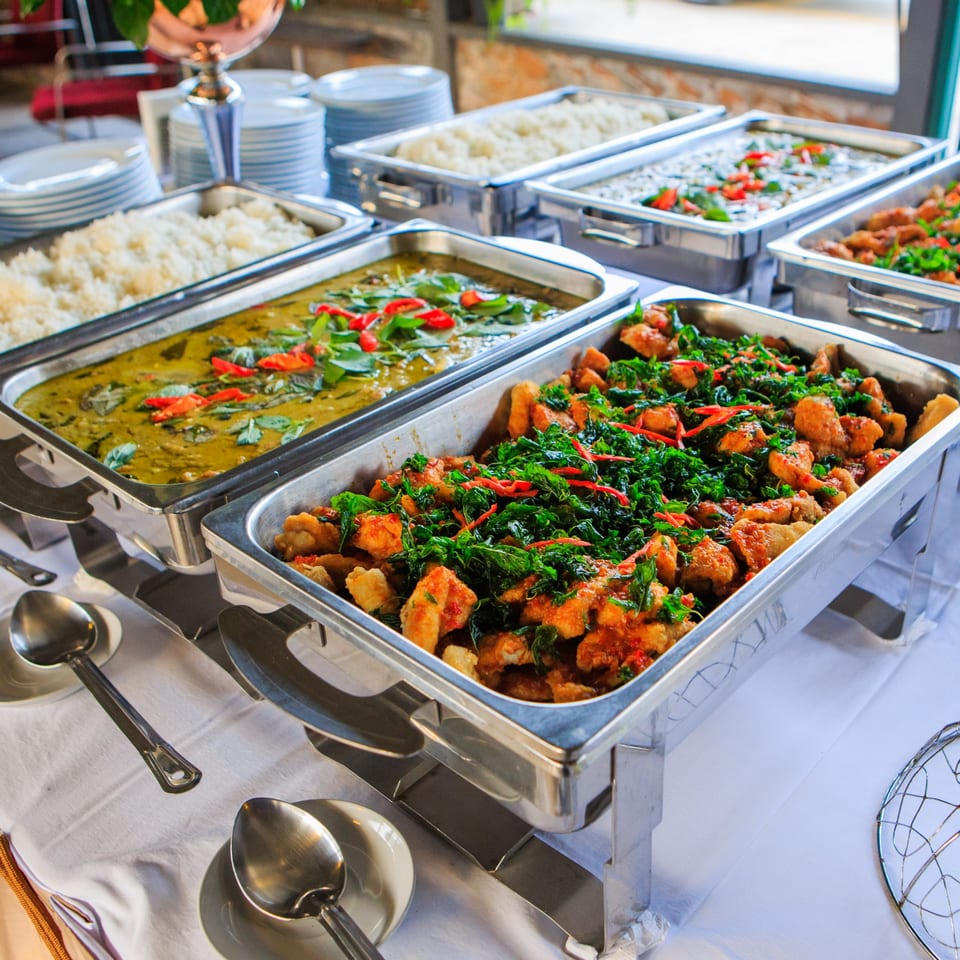 Buffet line with chafing dishes of green curry, rice, and a stir-fry with basil and chilies.