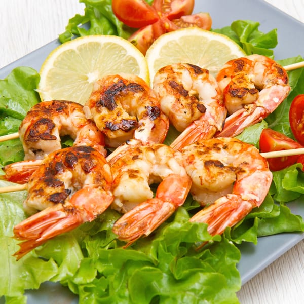 Grilled shrimp skewers on a bed of lettuce with lemon slices and cherry tomatoes.